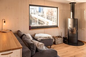 Un intérieur moderne avec un plancher en bois, un canapé avec des coussins, une table en bois, une grande fenêtre donnant sur un pont et un poêle noir.