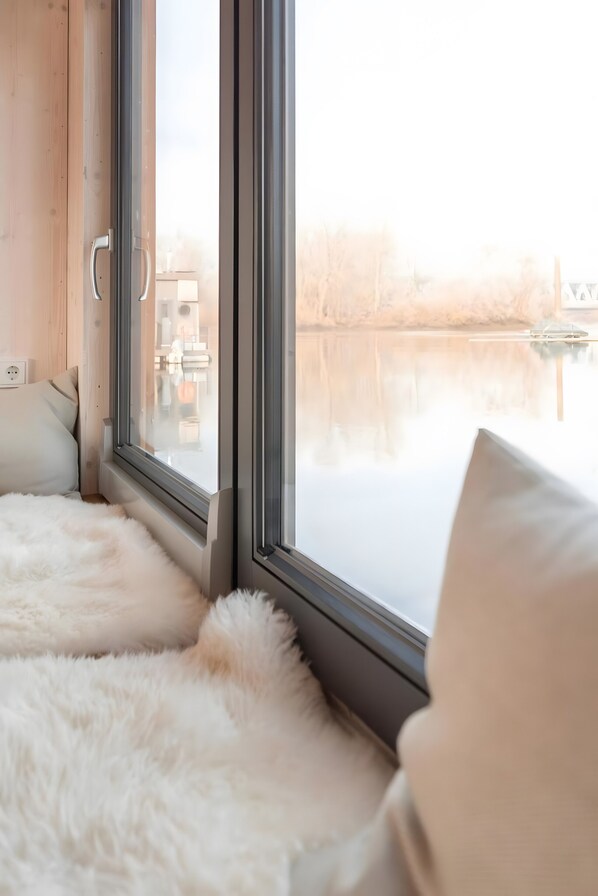 Une pièce avec une grande fenêtre, un tapis blanc et moelleux, et un coussin blanc.