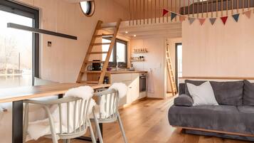 Eine moderne Küche mit Holzvertäfelung, ein Essbereich mit einem weißen Stuhl und ein graues Sofa.