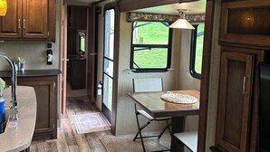 Eine kleine Wohnmobilküche mit Holzausbau, Spüle und einer Essecke mit Tisch und Stühlen.
