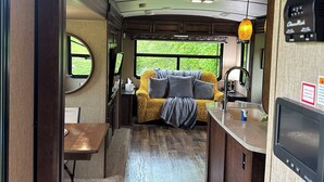 Ein kompaktes Wohnmobil-Interieur mit Küchenzeile, Essbereich und einer Sitzecke mit Sofa und Fenster.