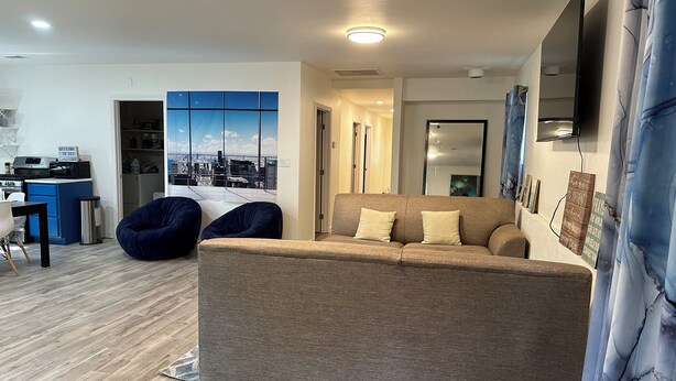 Een moderne woonkamer met een bank, een eethoek met tafel en stoelen, een keuken en een groot raam met uitzicht op de stad.