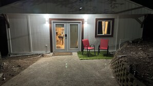 Een laag gebouw met een voordeur, twee rode stoelen en een klein terras.