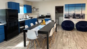 Een moderne keuken met blauwe kastjes, een zwarte koelkast, en een eethoek met een tafel en stoelen.