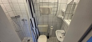 A small bathroom with a toilet, sink, and shower. - Room 'Doppelzimmer 2' with Shared Terrace, Private Garden and Wi-Fi (Cuxhaven)