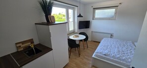 A compact room with a kitchenette, a dining area with a table and chairs, a bed, and a TV mounted on the wall. - Room 'Doppelzimmer 2' with Shared Terrace, Private Garden and Wi-Fi (Cuxhaven)