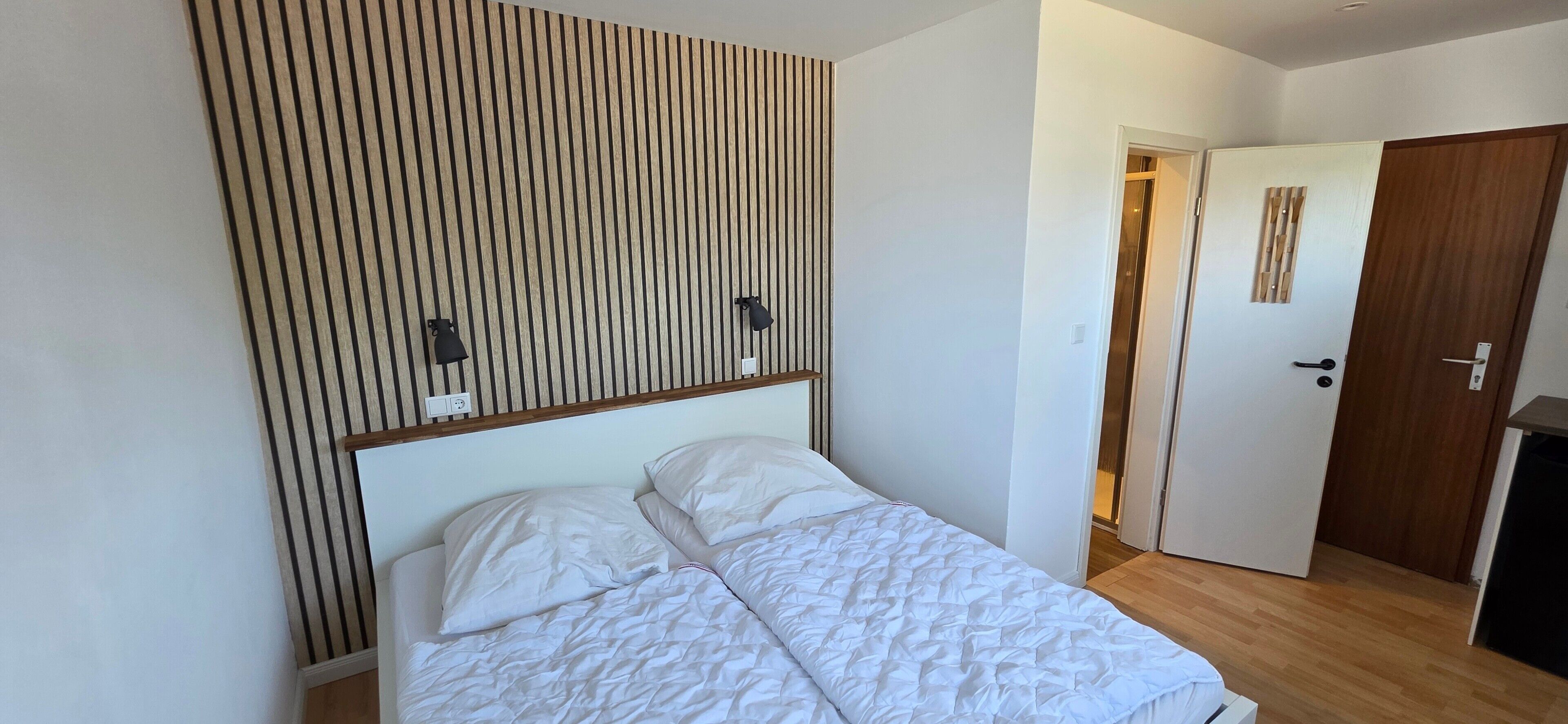 Une chambre à coucher avec un lit, un mur recouvert de lambris en bois, une porte et un interrupteur.