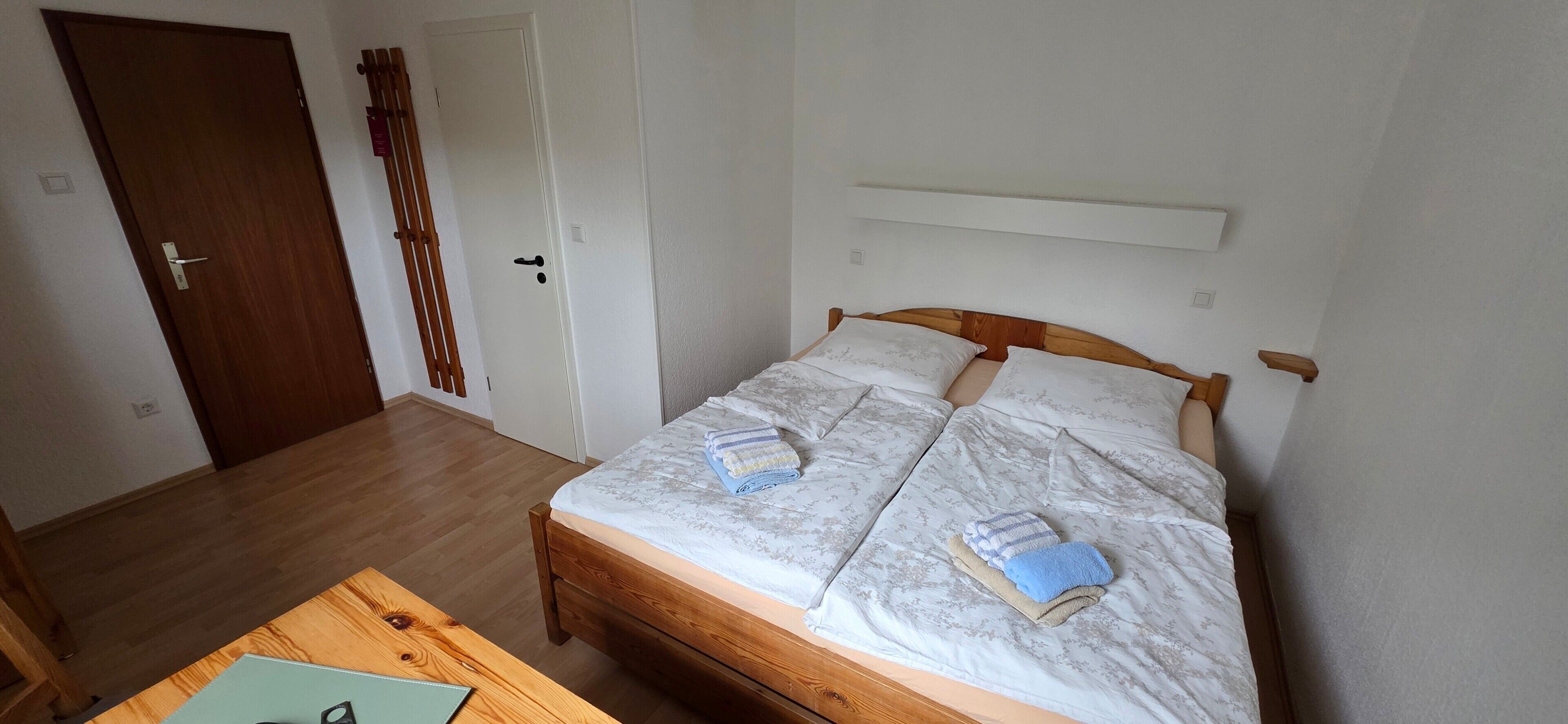 A room with a wooden bed, a desk with a chair, and a door.