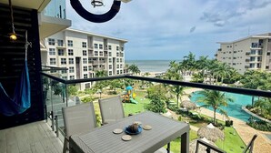 A balcony with a table and chairs, overlooking a swimming pool and a playground. - Beachfront Condo | Caracol Beach, Punta Chame | Pools & Ocean Views (Chame)
