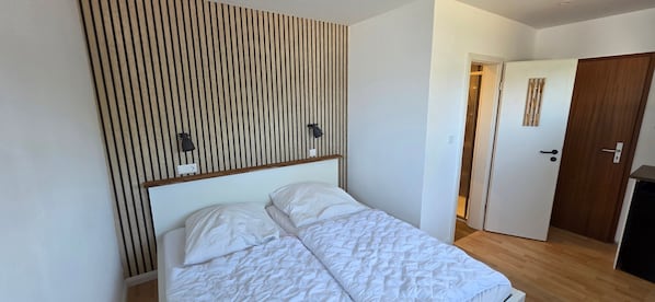 A bedroom with a bed, a wooden slat wall, a door, and a light switch.