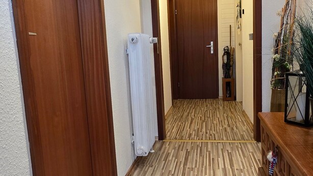 A hallway with wooden flooring, a radiator, and a door leading to another room.