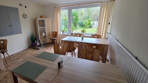 A dining area with a wooden table and chairs, a cabinet with glass doors, and a view of the garden through large windows.