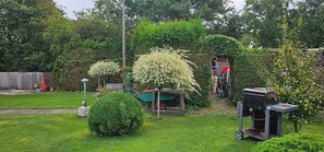A well-maintained garden with a variety of plants, a barbecue grill, and a green wheelbarrow. - Apartment '3 Im Eg' with Wi-Fi (Cuxhaven)