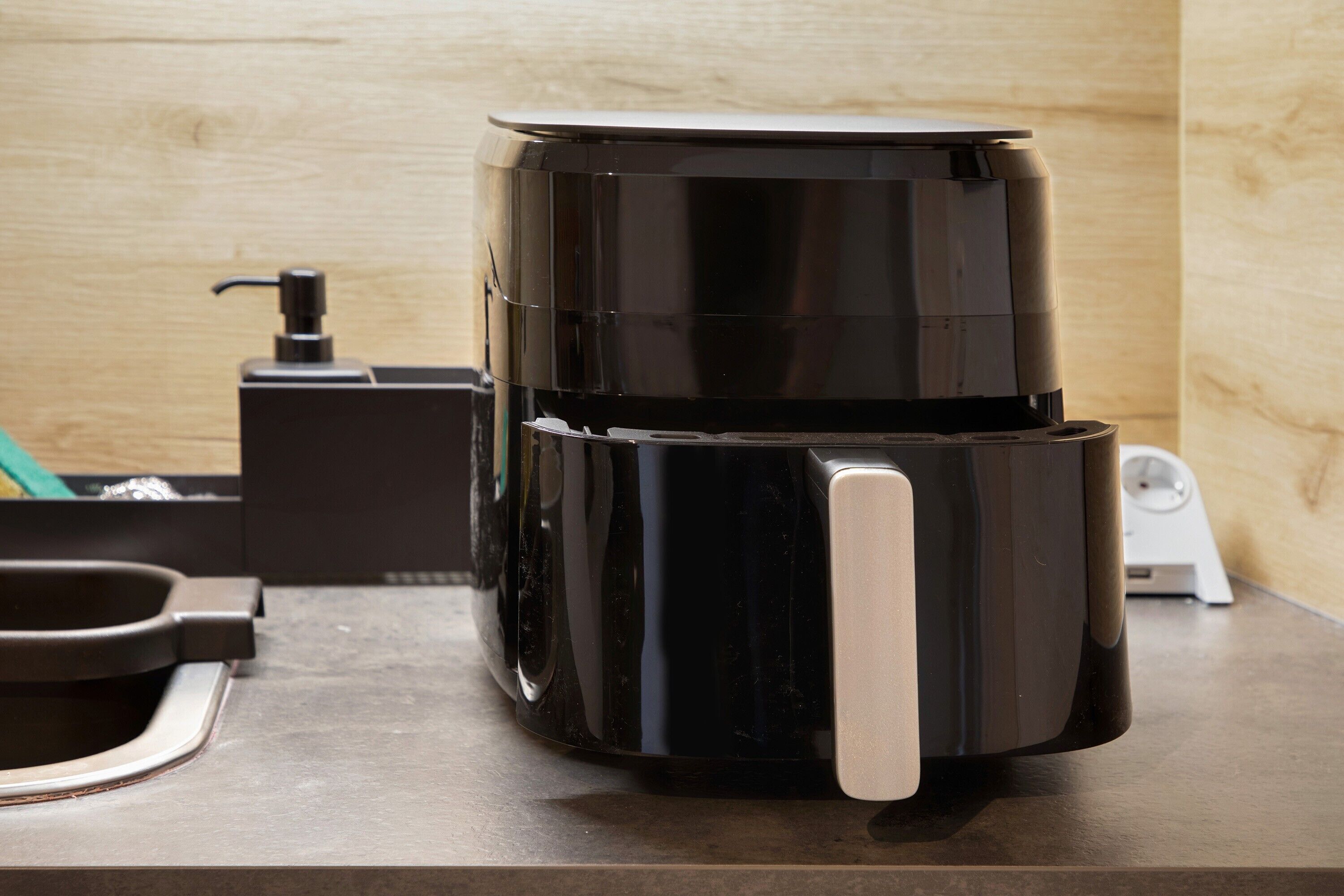 A black coffee maker on a countertop with a pump dispenser, a small black box, and a white power outlet.