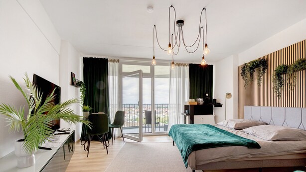 A modern bedroom with a bed, desk, chair, and a balcony with a view.