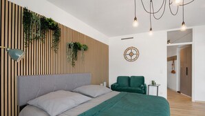 A modern bedroom with a bed, a green chair, a wall-mounted plant, a wall clock, and a hanging light fixture.