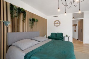 A modern bedroom with a bed, a green chair, a wall-mounted plant, a wall clock, and a hanging light fixture.