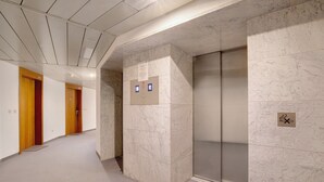 A hallway with marble walls, wooden doors, and an elevator.
