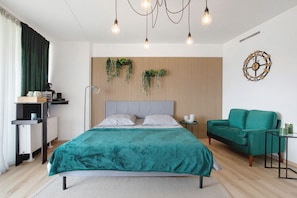 Une chambre moderne avec un lit, un canapé vert, une table de chevet, une horloge murale et un luminaire suspendu.