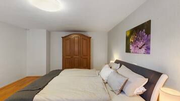 A bedroom with a large bed, a wooden wardrobe, and a wall-mounted lamp.