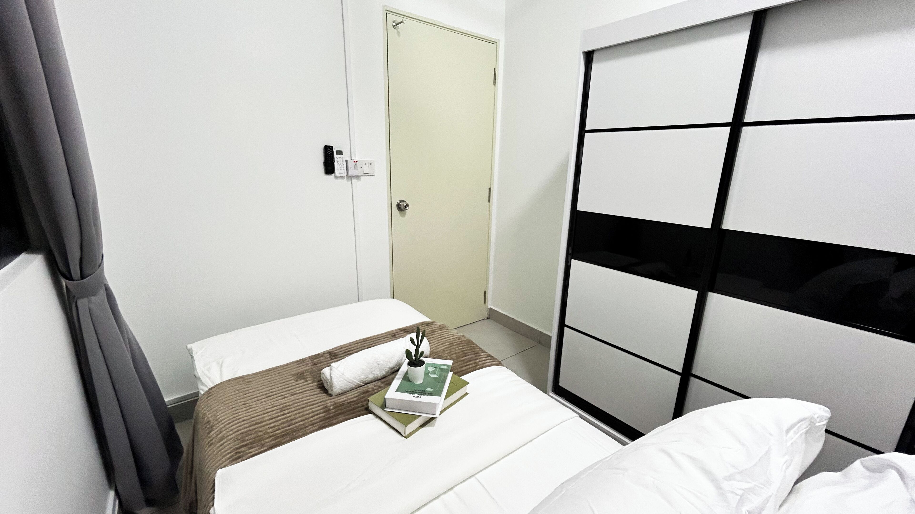 A hotel room with a bed, a bedside table, a nightstand, a door, and a wardrobe.