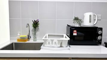 Eine Küche mit Spüle, Mikrowelle, Kaffeemaschine, einer Handseifenflasche, einem Schwamm und einer kleinen Pflanze.