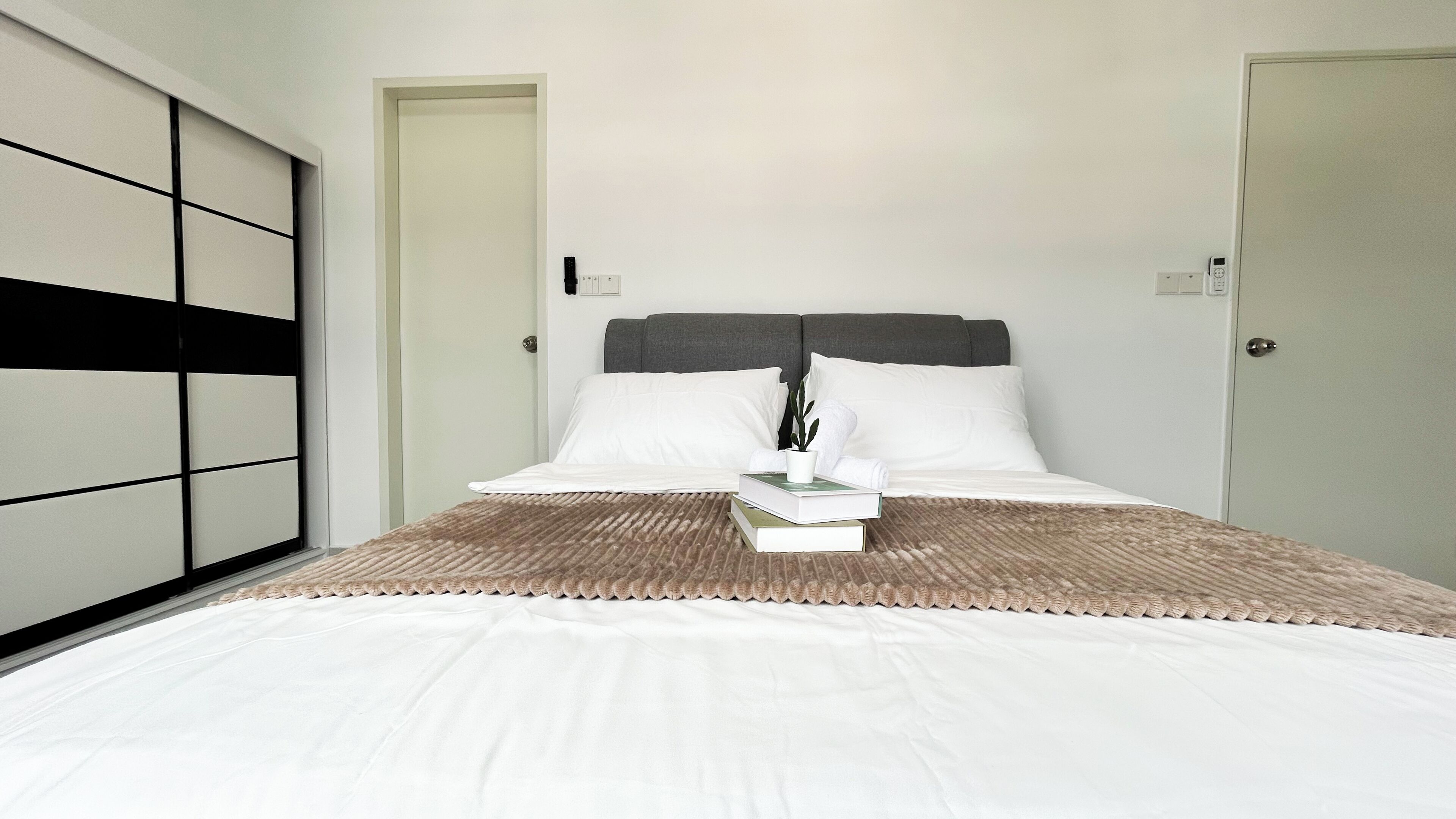 A neatly made bed with white linens, a grey headboard, and a brown textured blanket. There is a small potted plant on the bed.