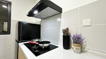 Una cocina con tope de inducción negro, una olla encima, una campana extractora negra, un portavasos con cuchillos y un florero decorativo con lavanda.
