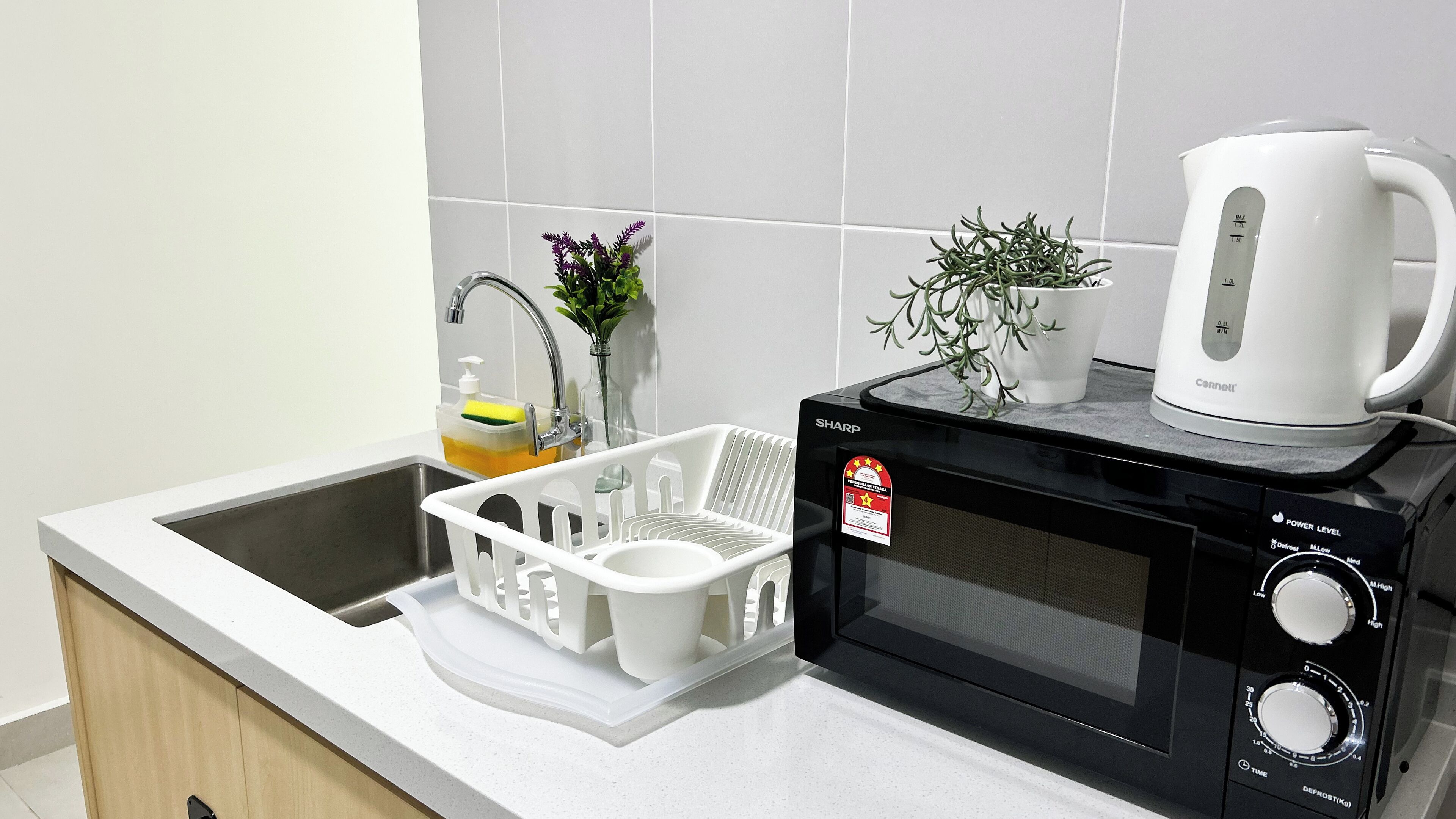 A kitchen with a microwave, kettle, and a dish rack.