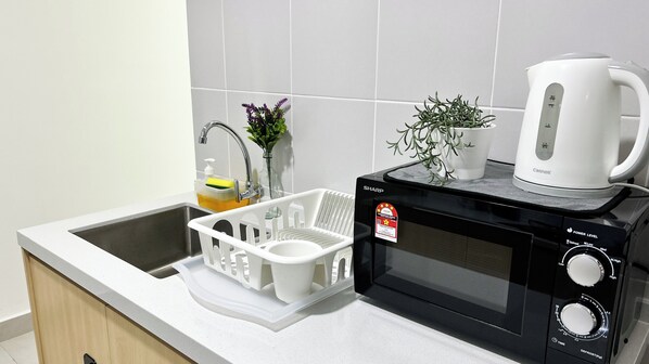 Una cocina equipada con microondas, hervidor y escurreplatos.