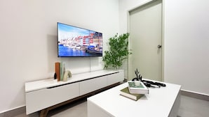 A modern living room with a flat-screen TV displaying a cityscape, a white console table with books and a plant, and a door to the right. - 168 Park Selayang by Manhattan Group (Batu Caves)