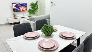 A modern dining area with a white table set for four, a potted plant in the center, and a flat-screen TV mounted on the wall. - 168 Park Selayang by Manhattan Group (Batu Caves)