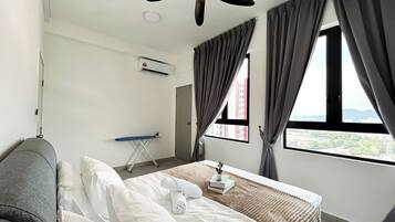 A hotel room with a bed, a window with curtains, an ironing board, and a wall-mounted air conditioner.