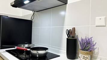 A modern kitchen with a black induction cooktop, a stainless steel pan, and a black pot on the cooktop. There is a black pot lid on the counter. A black pot is on the stove. A black pot is on the counter.