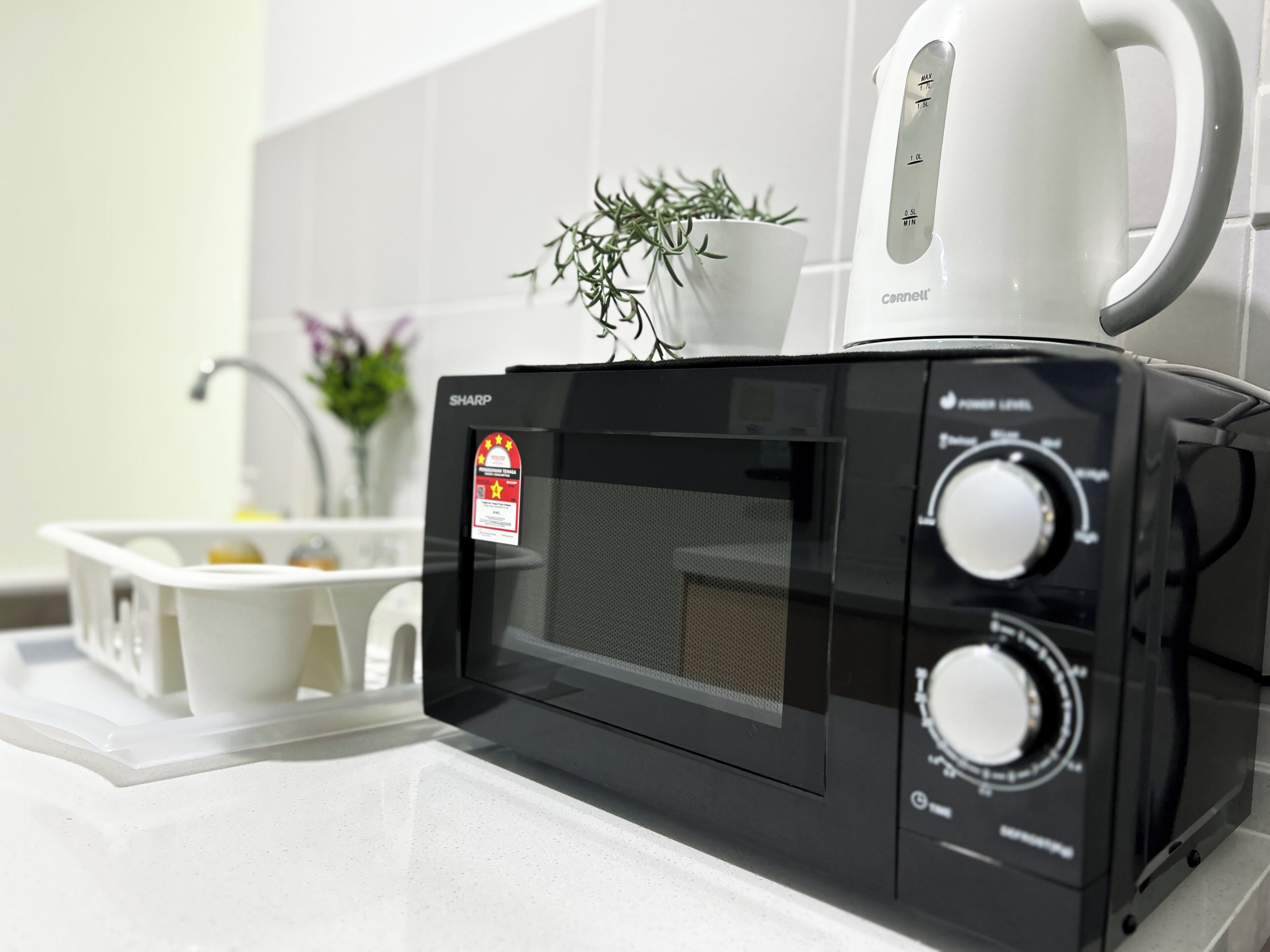 A black Sharp microwave oven with a digital display and control knobs, placed on a white countertop in a kitchen.