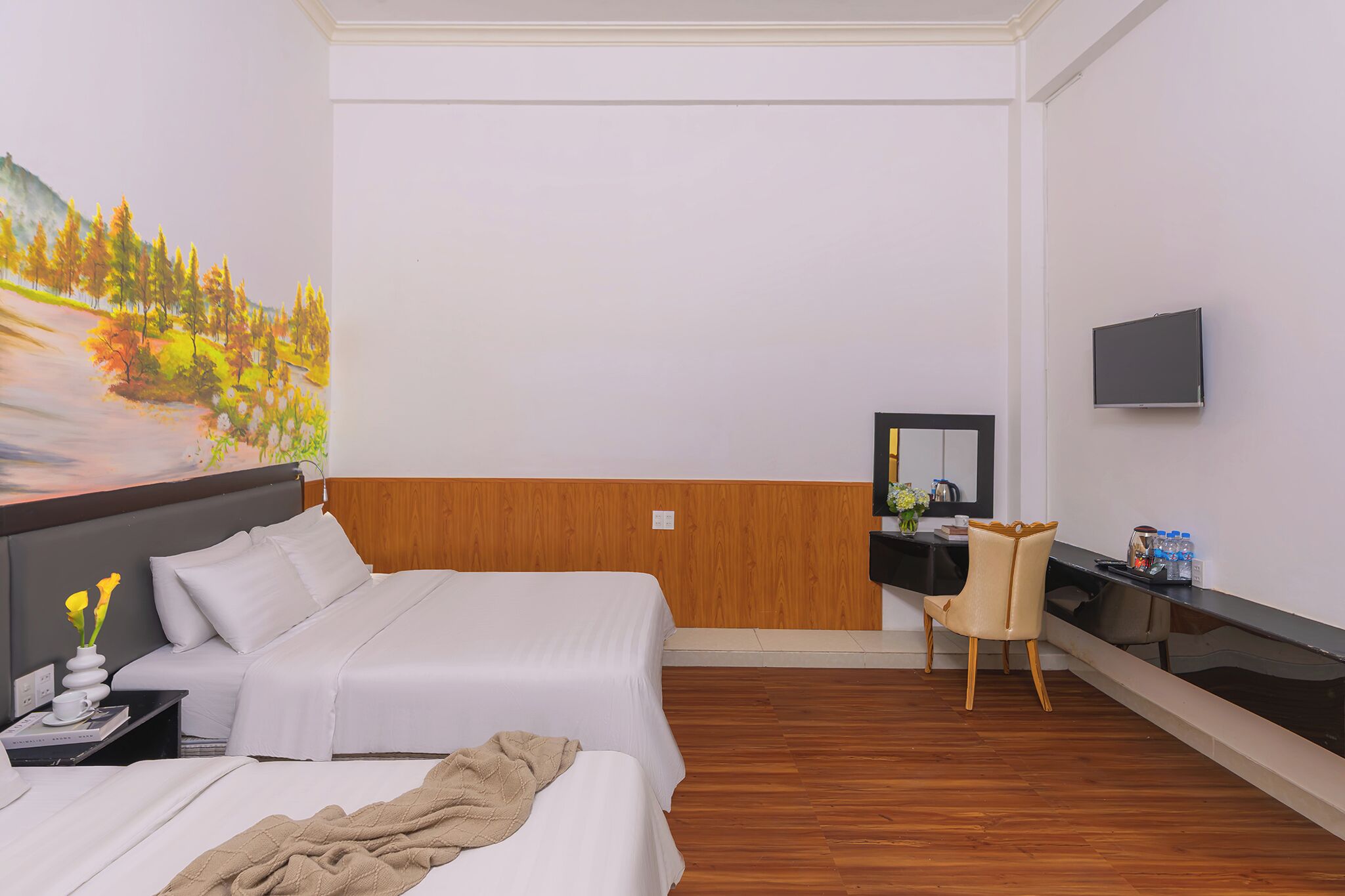 A hotel room with two beds, a wooden accent wall, a desk with a chair, a flat-screen TV, and a painting of a landscape.