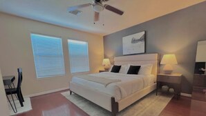 A bedroom with a bed, two bedside lamps, a ceiling fan, and a window with blinds.
