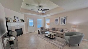 A spacious living room with a fireplace, a ceiling fan, and a large window.