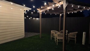A covered patio area with string lights, two wicker chairs, and a white column.