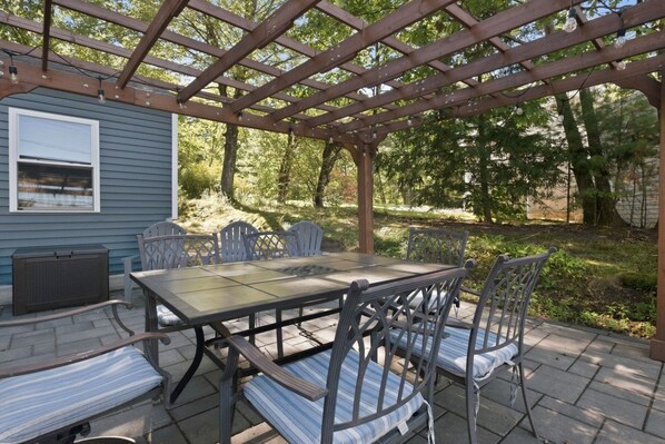 Un patio exterior con pérgola, una mesa, sillas y un área cubierta.