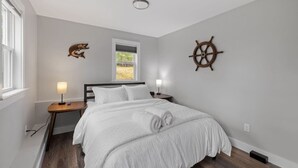 Ein Schlafzimmer mit einem Bett, zwei Nachttischen, einem Fenster und einem an der Wand befestigten Schiffsschwungrad.