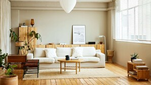 Ein modernes Wohnzimmer mit Sofa, Couchtisch und Beistelltischen. Es gibt ein großes Fenster mit Jalousien, eine Hängelampe und ein gerahmtes Bild an der Wand.