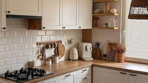 Eine moderne Küche mit weißen Schränken, einem Gasherd und Holzarbeitsplatten. Ein Essbereich mit Korbstühlen und einem Tisch.