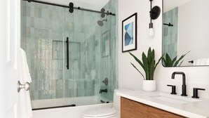 Ein modernes Badezimmer mit Duschkabine aus Glas, einer weißen Toilette, einem Holzwaschtisch und einer Zimmerpflanze.