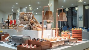 Mostrador de panadería con diversos panes y pasteles, una máquina de café e iluminación decorativa.