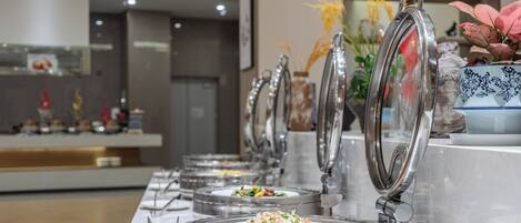 Un buffet composé de plusieurs présentoirs de nourriture, chacun étant équipé d’un plat de service couvert et de couverts.