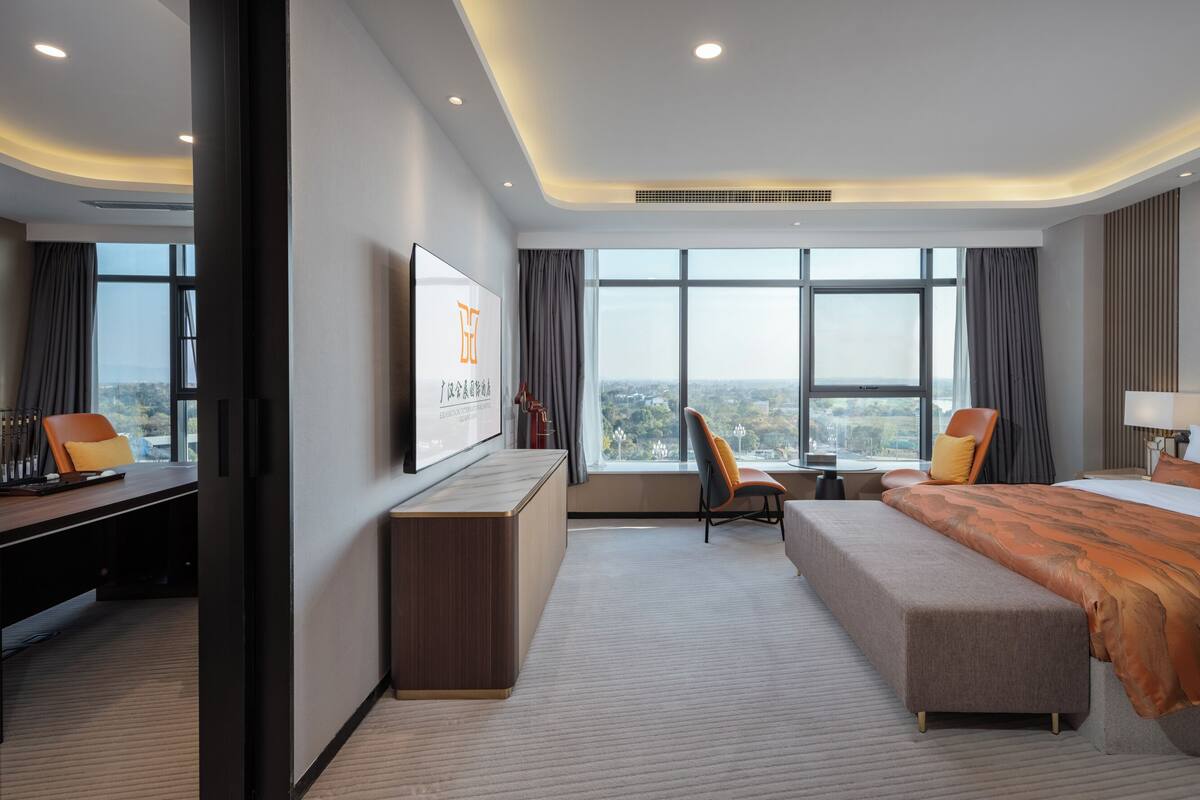 Ein modernes Hotelzimmer mit einem großen Bett, einem Schreibtisch, einem Fernseher und Blick auf die Stadt.
