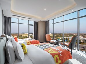 Een hotelkamer met twee bedden, een bureau en een stoel. De kamer heeft grote ramen met uitzicht op de stad.