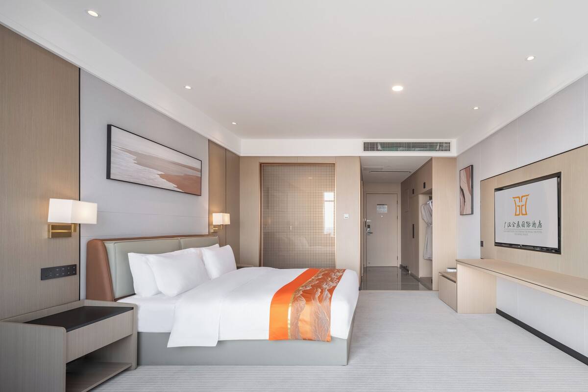 Ein modernes Hotelzimmer mit einem großen Bett, Nachttischen, einem Schreibtisch und Blick auf den Flur.