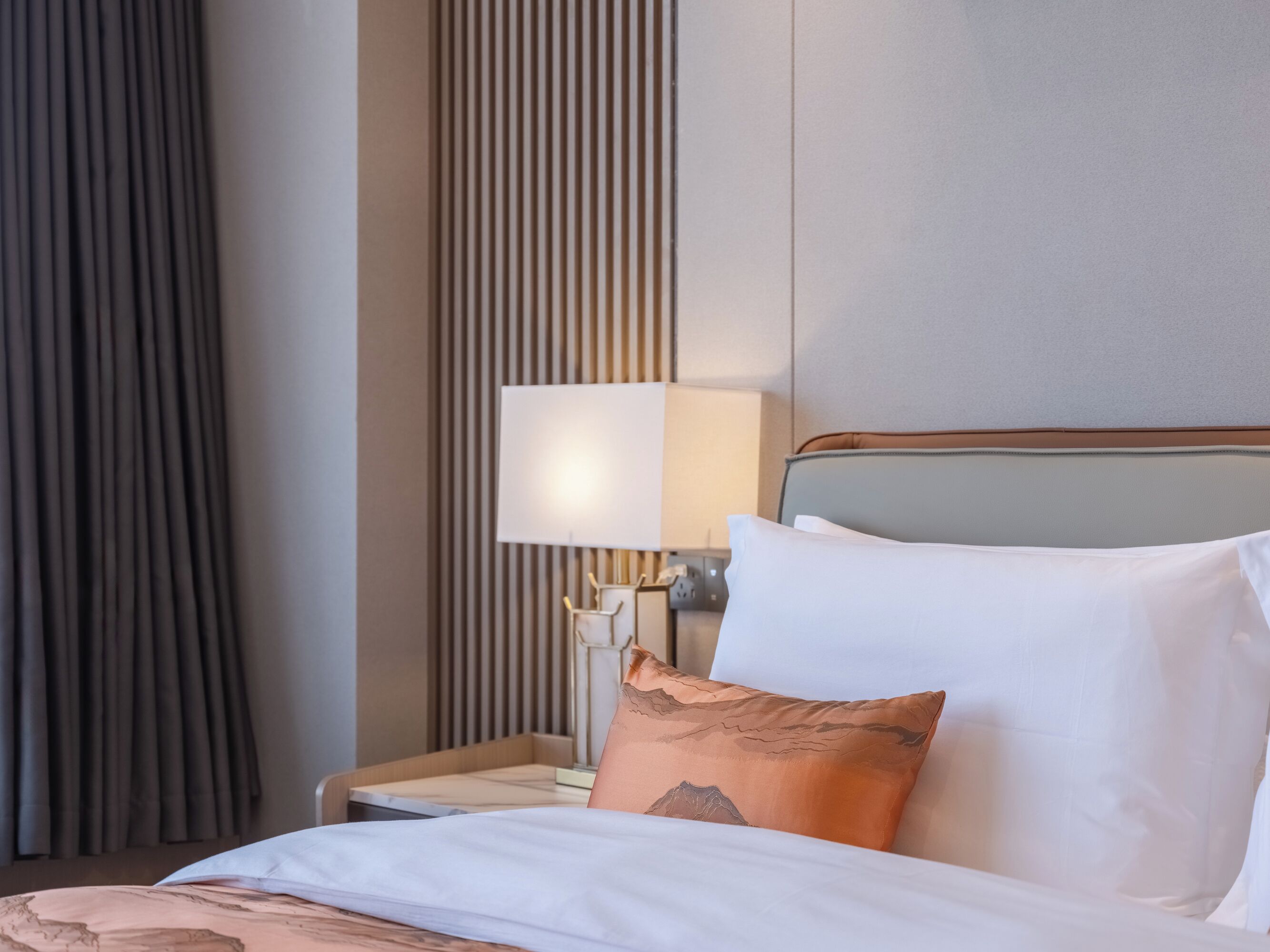Une chambre d’hôtel avec un lit, une table de chevet, une lampe et une fenêtre avec des rideaux.